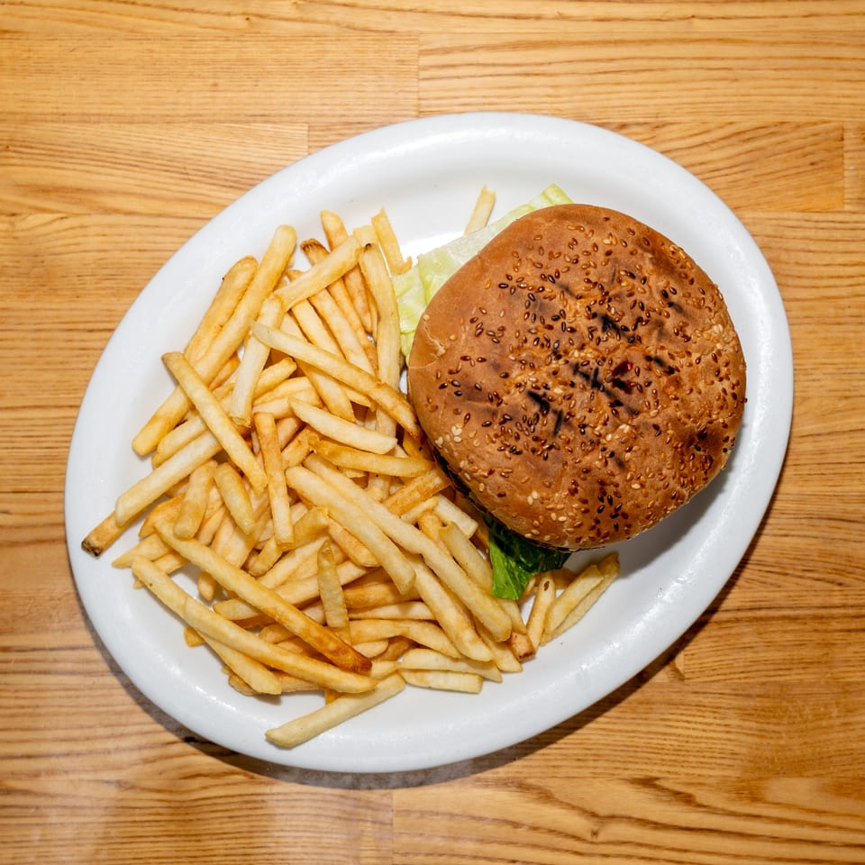 Sesame-seed burger with lettuce and French fries served on a white plate over a wooden table.