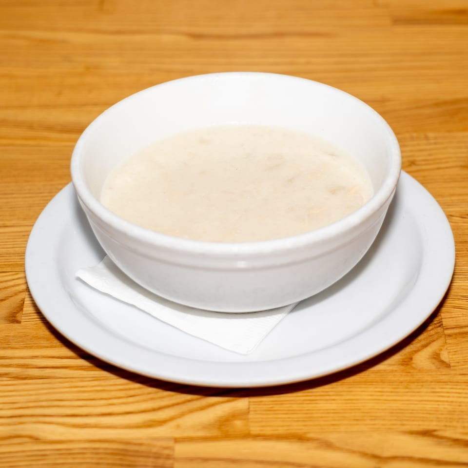 Bowl of creamy soup served on a white plate with a napkin on a wooden restaurant table.