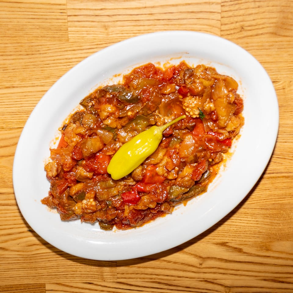 Rustic vegetable stew with tomatoes, peppers, and onions served on a white plate, topped with a yellow chili pepper.