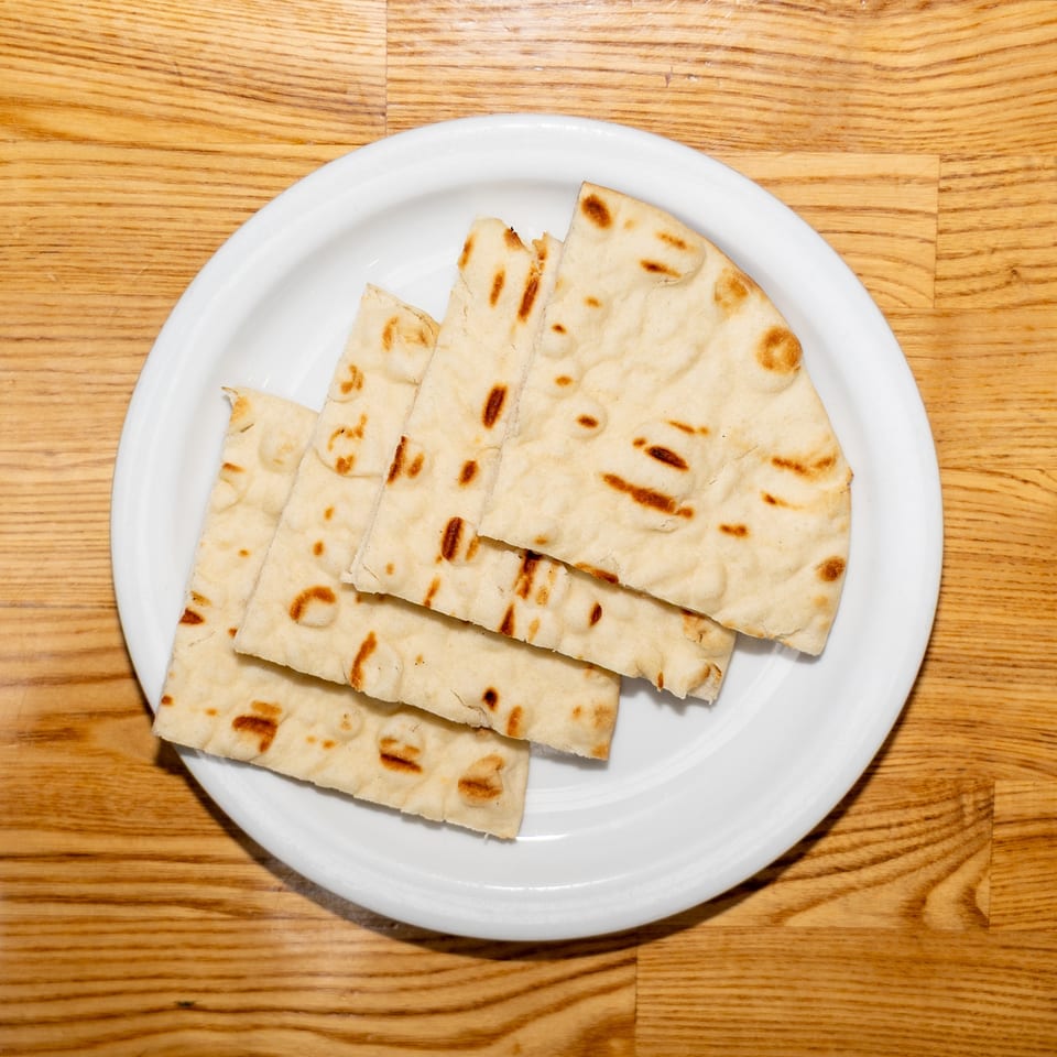 Grilled flatbread pieces arranged on a white plate atop a wooden table.