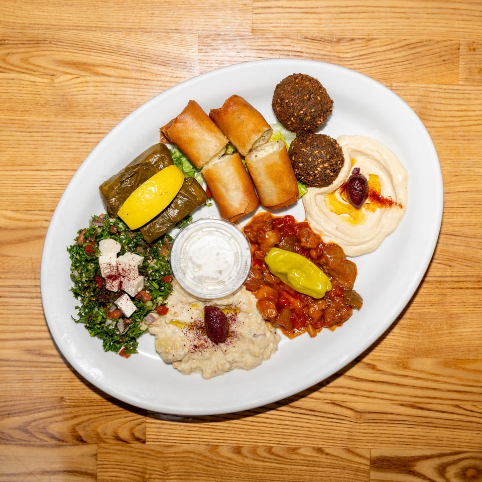 Middle Eastern mezze platter featuring hummus, falafel, stuffed grape leaves, spring rolls, tabbouleh, baba ghanoush, and vegetables.