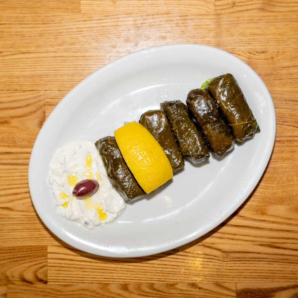 Stuffed grape leaves served with lemon, creamy yogurt sauce, and an olive on a white plate.