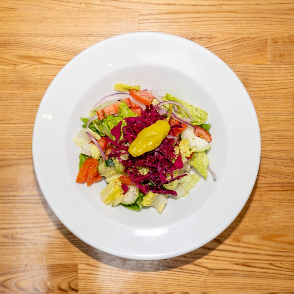 Fresh mixed salad with lettuce, tomatoes, cucumbers, onions, purple cabbage, and yellow pepper on a white plate.