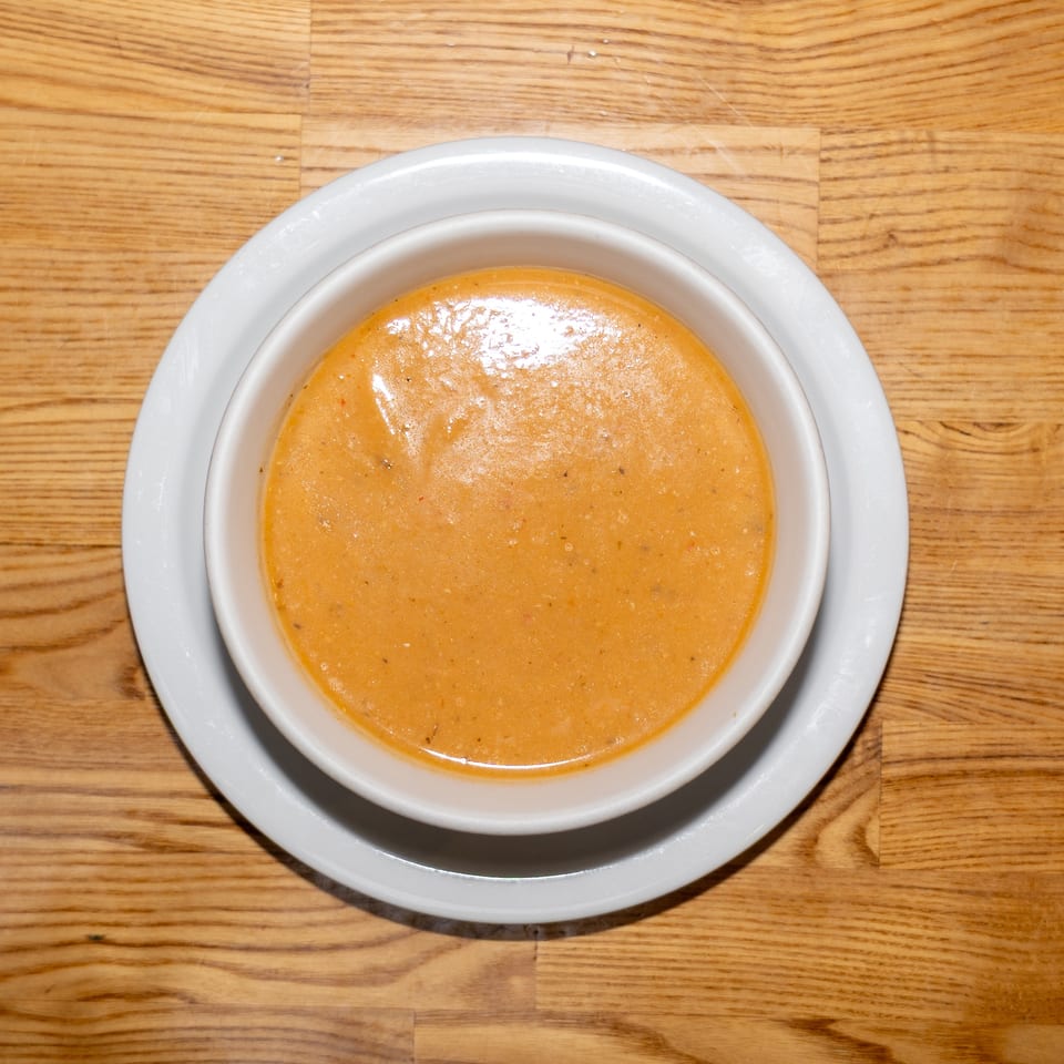 Bowl of creamy orange soup on a white plate atop a wooden table.