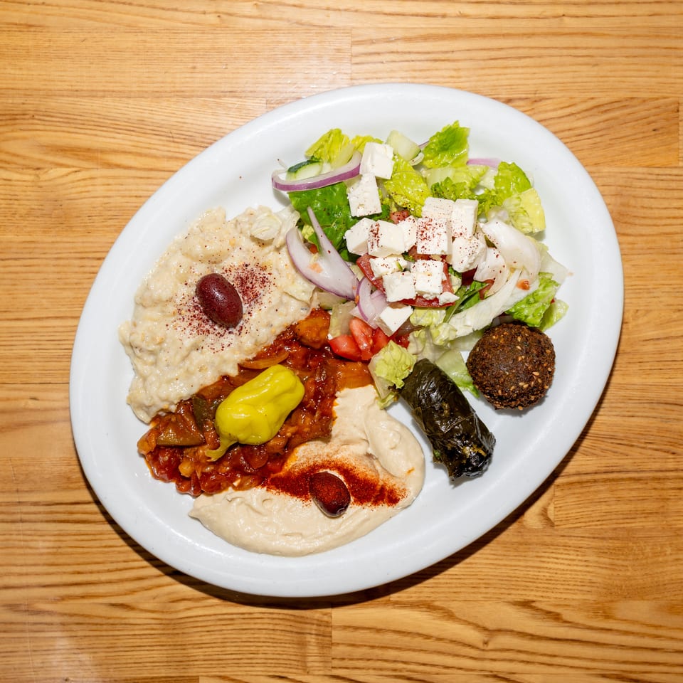 Mediterranean mezze platter with hummus, baba ghanoush, tabbouleh, feta salad, falafel, stuffed grape leaf, and pickled peppers.