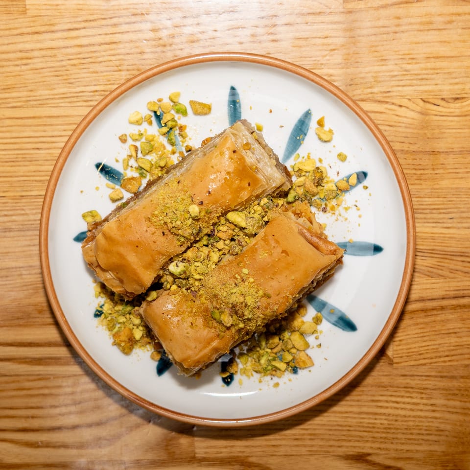 Golden baklava pieces topped with crushed pistachios on a decorative plate atop a wooden table.
