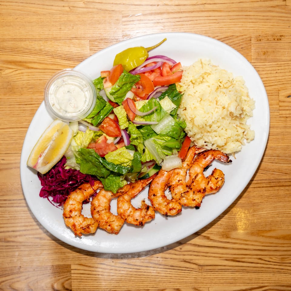 Grilled shrimp served with rice, fresh salad, red cabbage, lemon wedges, pickled pepper, and creamy dipping sauce.