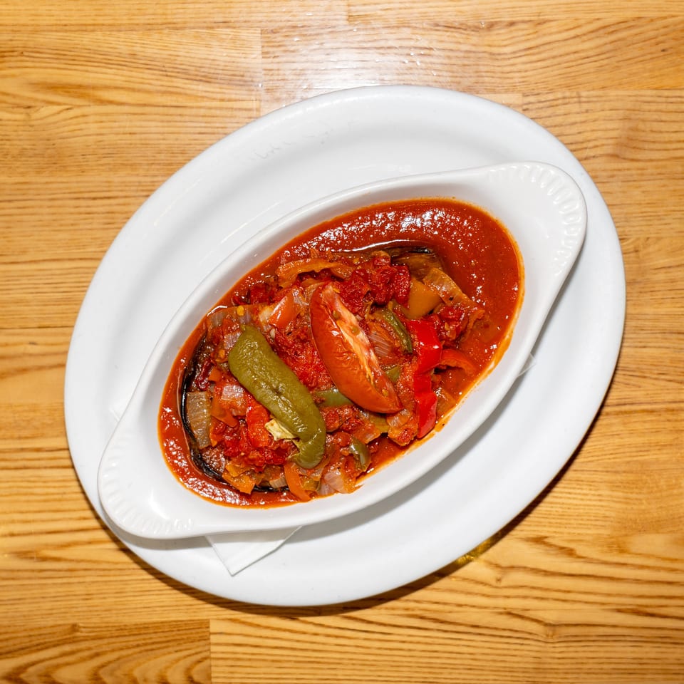 Vegetable stew with tomatoes, peppers, onions, and eggplant in red sauce, served in a white dish on a wooden table.