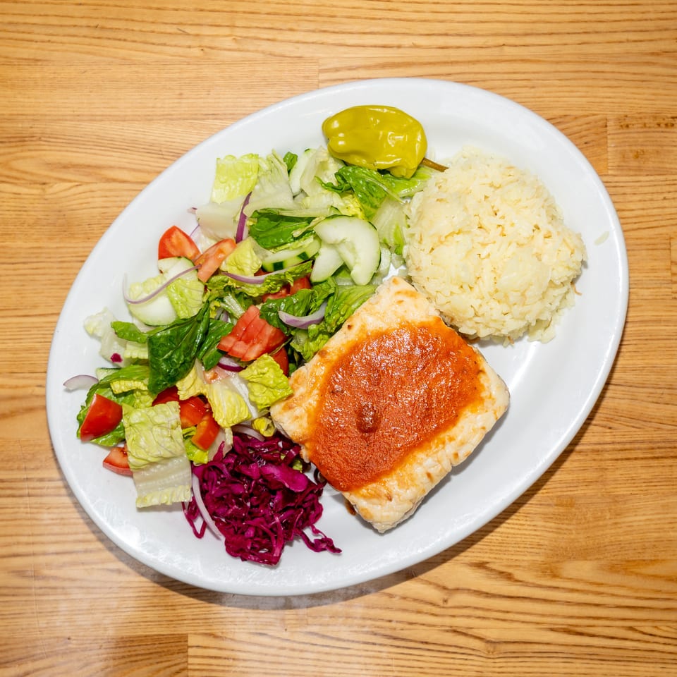 Plate of seasoned grilled chicken, rice, mixed salad, pickled cabbage, and a yellow pepper on a wooden table.