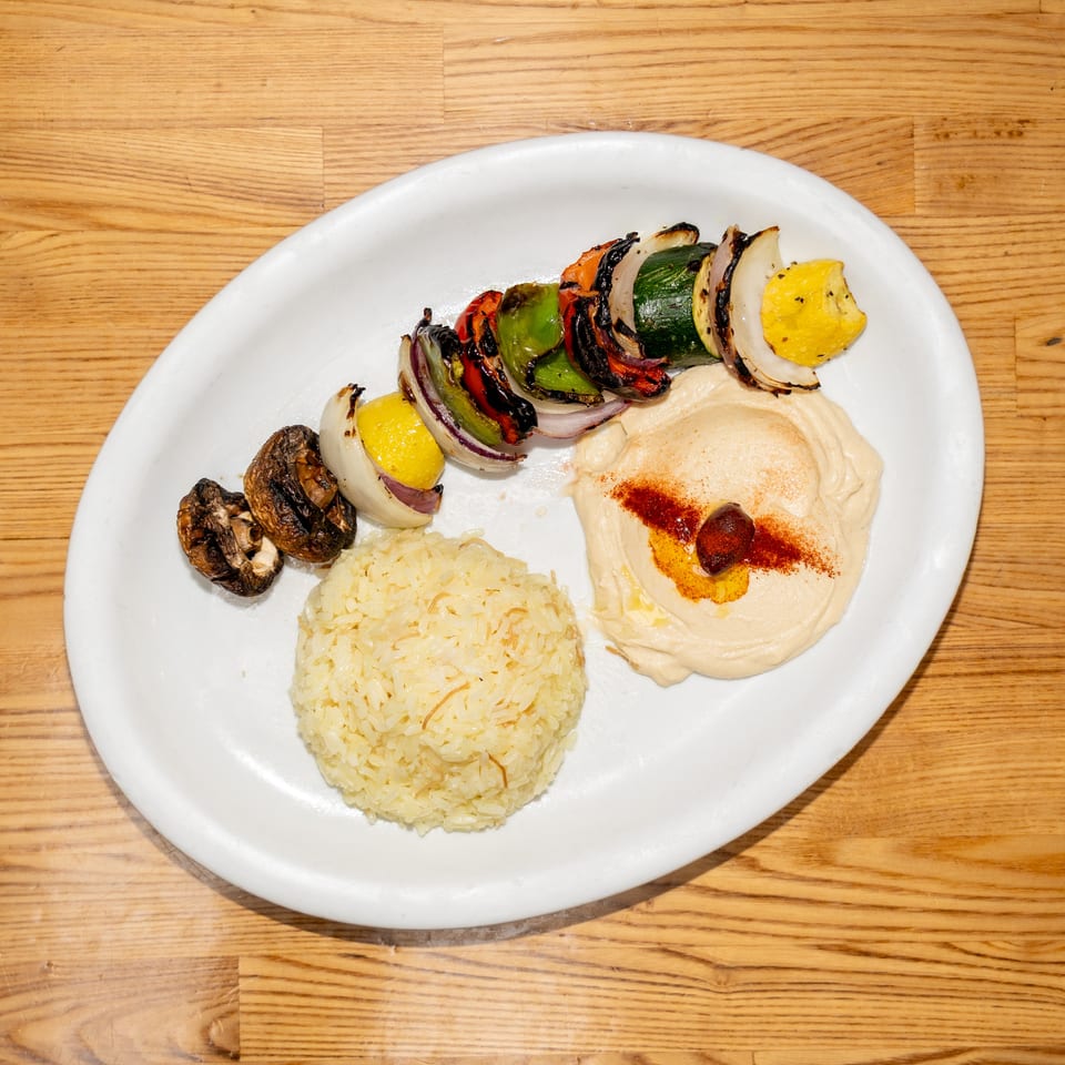 Plate of grilled vegetables, mushrooms, rice, and hummus topped with paprika and a chickpea on a wooden table.