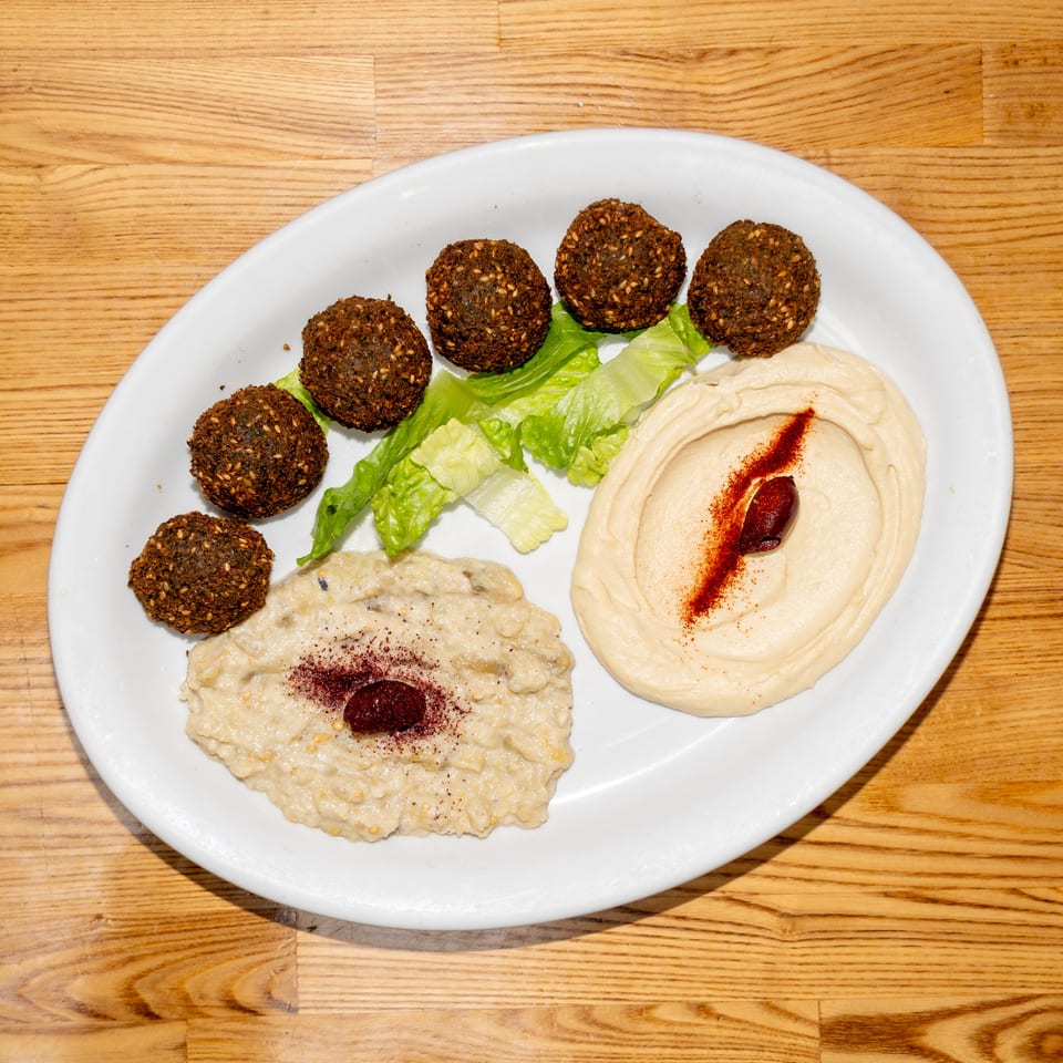 White plate of falafel, hummus, baba ganoush, and lettuce arranged on a wooden table.